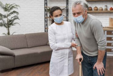 young beautiful woman with long wavy hair wearing apron and rubber gloves holding rug and cleaning spray looking confident and positive smiling showing thumbs up ready to clean standing over blue b