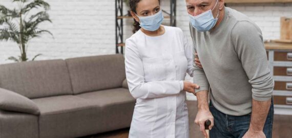 young beautiful woman with long wavy hair wearing apron and rubber gloves holding rug and cleaning spray looking confident and positive smiling showing thumbs up ready to clean standing over blue b