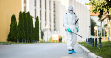 Disinfectant worker in protective suit sanitizing empty city streets during COVID-19 epidemic.